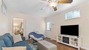 Una sala de estar con un sofá azul, un mueble blanco para el equipo de entretenimiento, un ventilador de techo y un televisor.