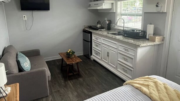 A compact living space with a kitchenette, a sofa, a small table, and a bed. - Tiny home Rental (Houston)