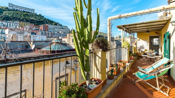 A rooftop terrace with a large cactus, potted plants, a table with chairs, and a view of a cityscape with buildings and a hill in the background. - Stylish in Spanish Quarter by Wonderful Italy (Naples)