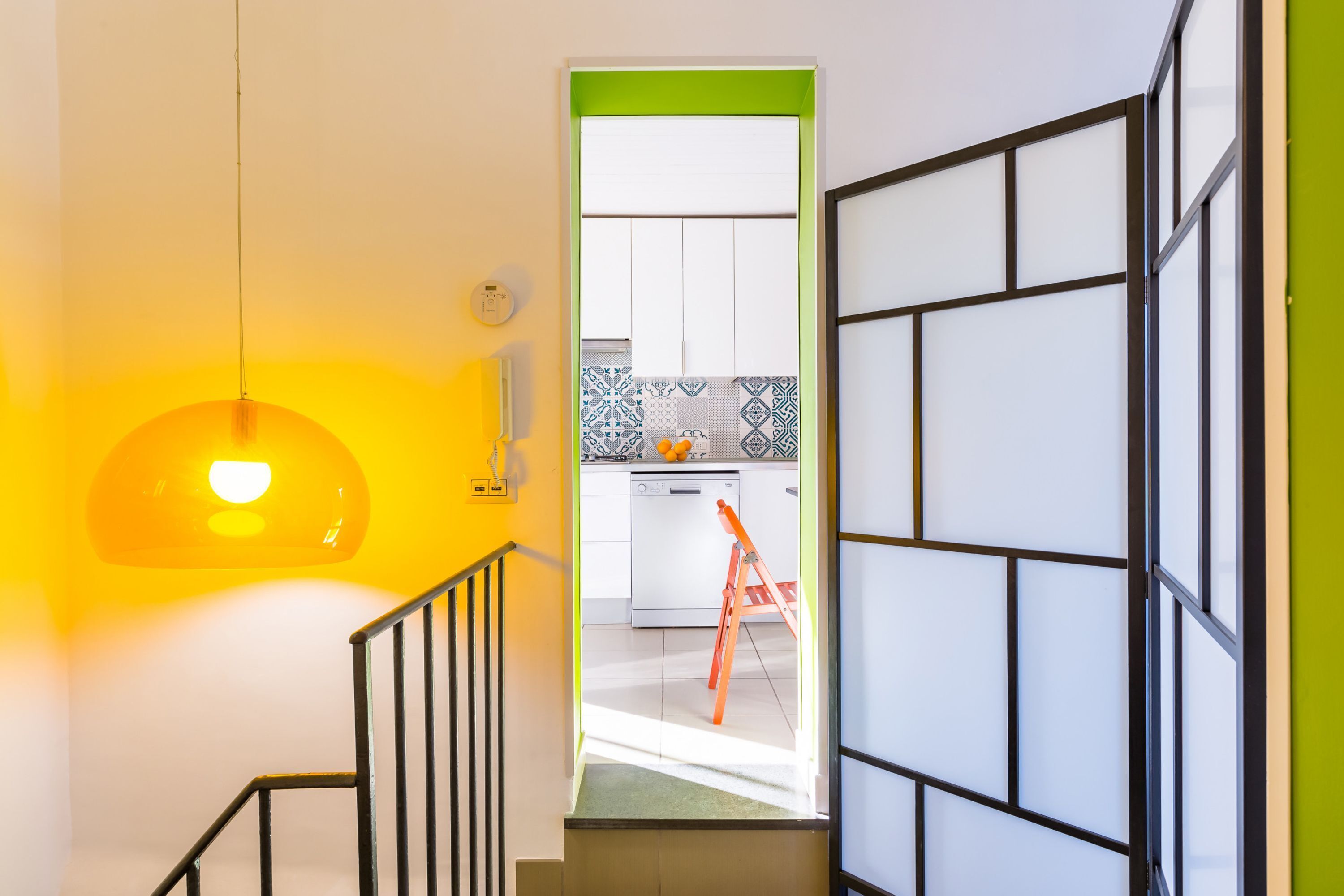 A staircase leading to a kitchen with white cabinets and a patterned backsplash.