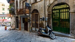 A narrow street with a scooter parked in front of a building with a green gate and a balcony with clothes hanging. - Stylish in Spanish Quarter by Wonderful Italy (Naples)