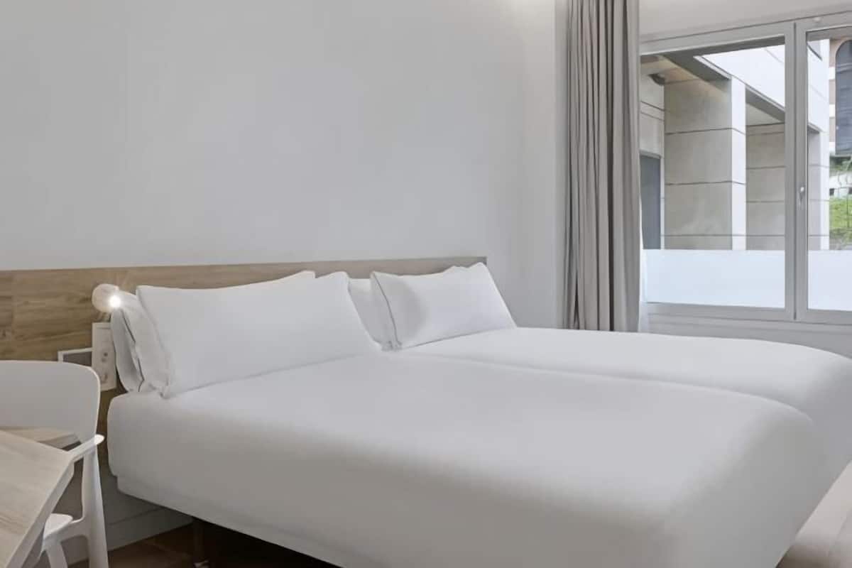 Une chambre d’hôtel avec un grand lit, une table de chevet et une fenêtre avec des rideaux.