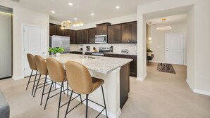 A modern kitchen with a central island, dark wooden cabinets, stainless steel appliances, and pendant lighting.