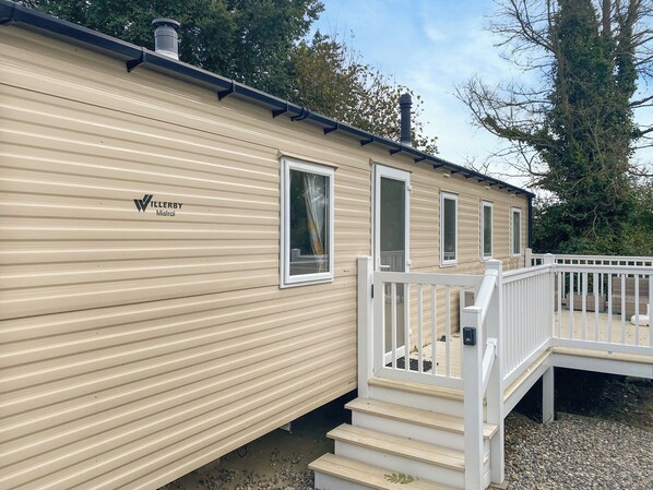 A mobile home with a beige exterior, a white deck, and a staircase leading to the entrance.