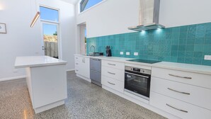 A modern kitchen with white cabinetry, a built-in oven, and a backsplash of teal tiles. - The Sunshine House - Nestled in the heart of the city. (Warrnambool)