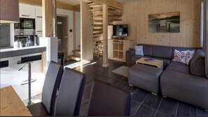 A modern living room with a grey sofa, a coffee table, and a TV. There is a staircase leading to a loft area with a TV and a wooden ceiling. - Attractive Chalet With Whirlpool (Sankt Georgen am Kreischberg)