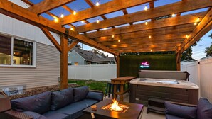 An outdoor patio with a wooden pergola, a fire pit, a hot tub, and a seating area with cushions. - Ultimate Group Getaway: Sleeps 16, Hot Tub, Arcade, & 5 Min from Mall of America (Minneapolis)