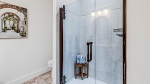 A modern bathroom with a glass-enclosed shower, a wooden stool, and a framed painting on the wall.