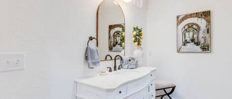 A bathroom with a white vanity, a large mirror, and a framed picture on the wall.
