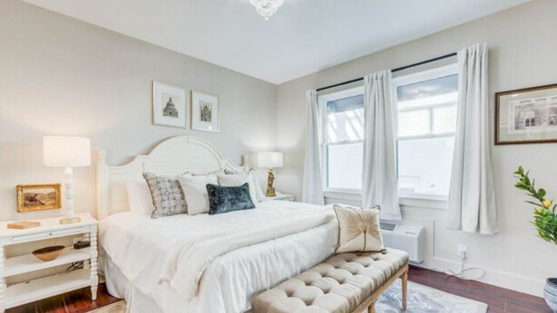 Une chambre à coucher avec un grand lit, des tables de chevet, un banc et une fenêtre avec des rideaux.