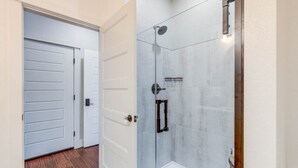 Un couloir mène à un espace de douche clos par des parois de verre, avec une porte sur le côté gauche.
