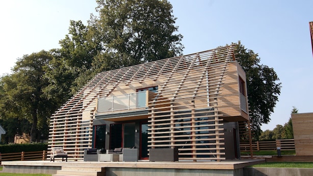 Una casa moderna con techo de listones, un porche cubierto y una pequeña zona de estar al aire libre.