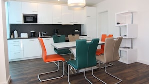 Una cocina moderna con armarios blancos, un microondas negro y un comedor con una mesa y sillas blancas.