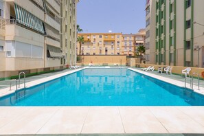 A rectangular swimming pool with clear blue water, surrounded by tiled flooring, and white lounge chairs. - Casa Marina - Apartment In Torre Del Mar (Velez-Malaga)