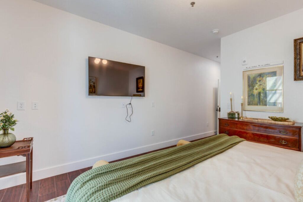 A bedroom with a bed, a dresser, a mirror, and a wall-mounted TV.