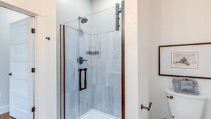 A bathroom with a glass-enclosed shower, a toilet, and a framed picture on the wall. - The Harbor Haven Room (Manteo)