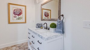 A bathroom with a white vanity, a mirror, and a framed floral artwork on the wall.
