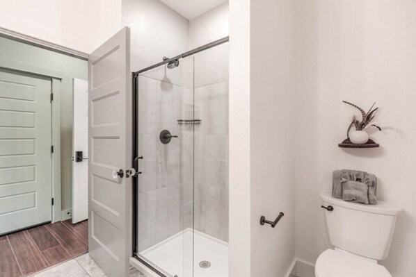 A bathroom with a glass-enclosed shower, a toilet, and a small shelf with a vase and towel.