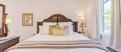 A neatly made bed with a wooden headboard, a bedside table with a lamp, and a window with curtains.