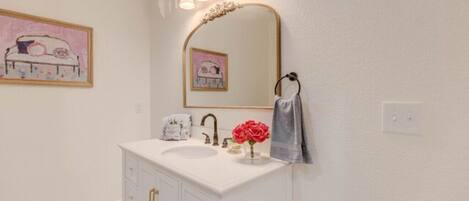 A bathroom with a white vanity, a large mirror, and a pink artwork on the wall.