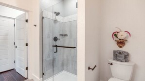 A bathroom with a glass shower enclosure, a toilet, and a towel rack. - The Blushing Rose Room (Manteo)