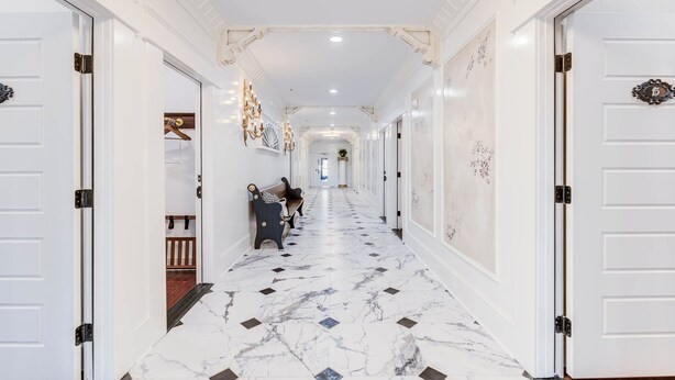 A hallway with marble flooring, white walls, and doors with ornate handles. - The Captains Quarters Room (Manteo)