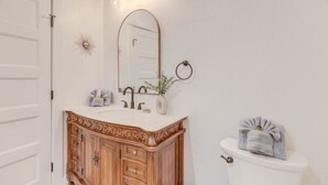 A bathroom with a wooden vanity, a white toilet, a mirror, and a wall-mounted towel rack. - The Captains Quarters Room (Manteo)