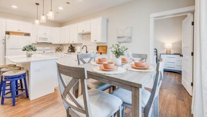 A modern kitchen with white cabinets, a central island, and a dining area with a table set for four. - Soundscape Family Suite/pet-friendly (Manteo)