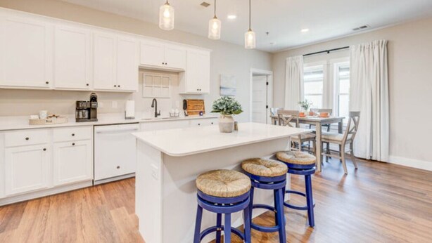 A modern kitchen with white cabinets, a central island, and blue barstools. - Soundscape Family Suite/pet-friendly (Manteo)