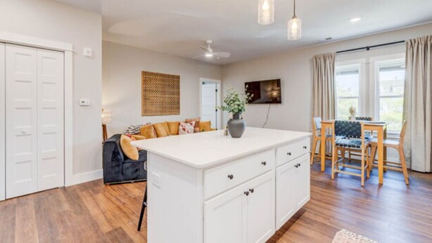A spacious kitchen with a central island, white cabinetry, and a dining area with a table and chairs. - The Downtown Delight Family Suite (Manteo)
