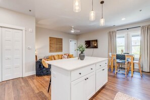 A spacious kitchen with a central island, white cabinetry, and a dining area with a table and chairs. - The Downtown Delight Family Suite (Manteo)