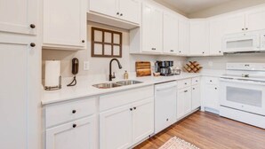 A modern kitchen with white cabinetry, a stainless steel sink, a microwave, and a stove. - The Downtown Delight Family Suite (Manteo)