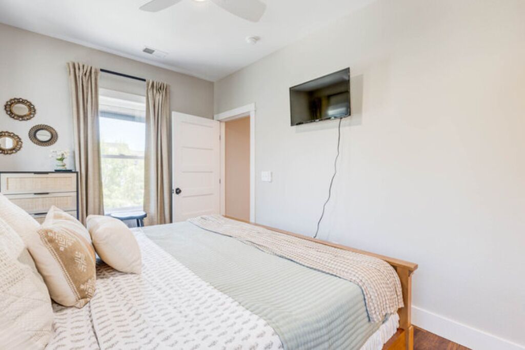 A bedroom with a bed, a dresser, a television mounted on the wall, and a window with curtains.