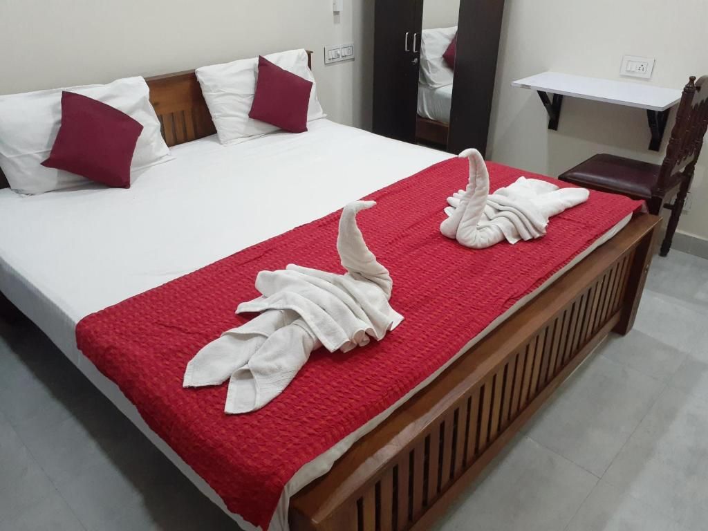 A hotel room with a bed, pillows, a red blanket, and towels arranged on the bed.