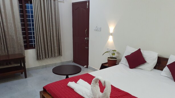 A hotel room with a bed, a small round table, a wooden bench, a potted plant, and a door. - NatureVilla Kochi (Aluva)