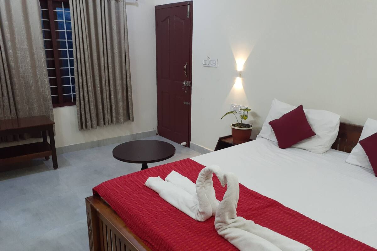 Habitación de hotel con cama, una mesita redonda, un banco de madera, una planta en maceta y una puerta.