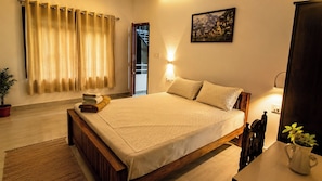 A bedroom with a bed, a bedside table, a lamp, a window with curtains, a door, and a wall-mounted picture. - NatureVilla Kochi (Aluva)
