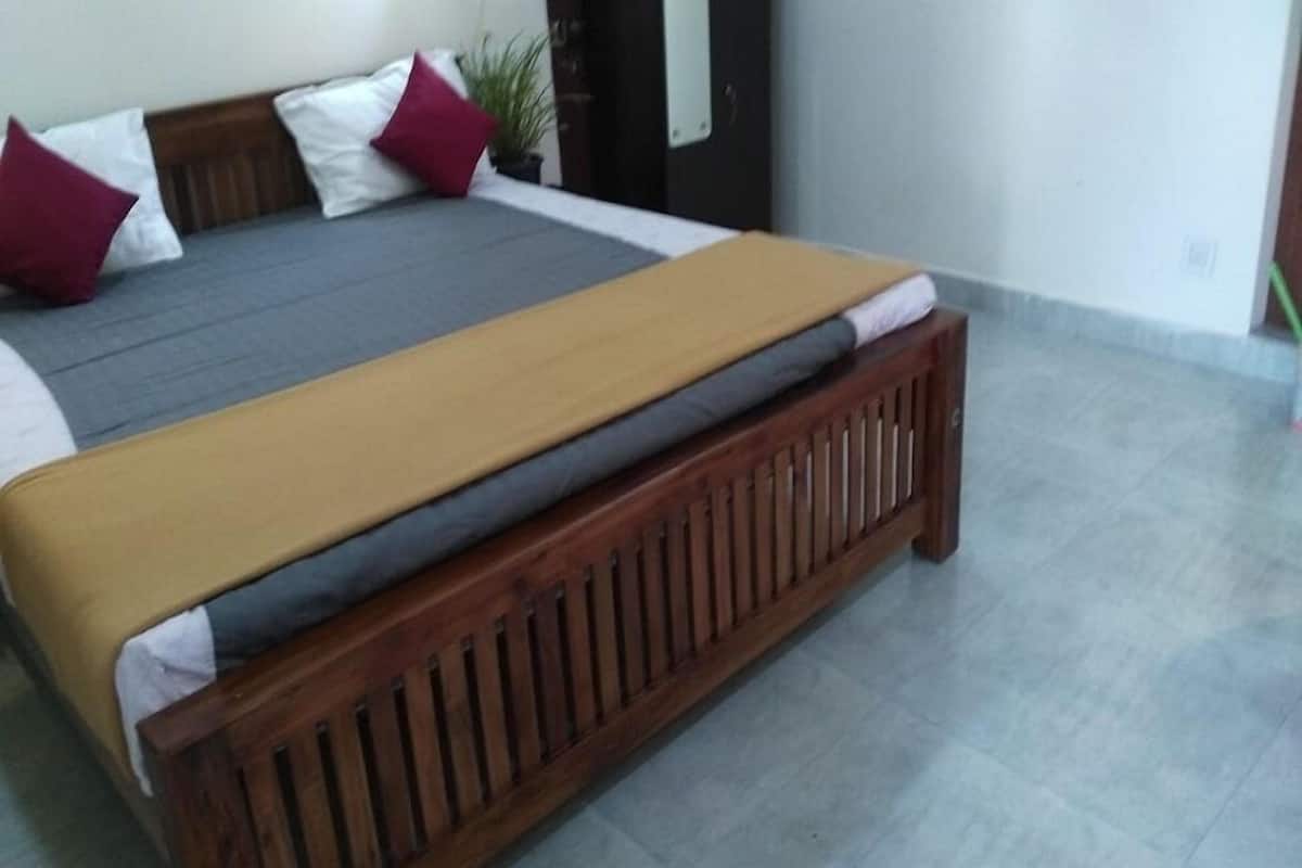Una cama con estructura de madera, ropa de cama gris y beige, y almohadas rojas y blancas.