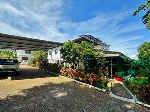 A residential property with a covered driveway, a two-story house, and a garden area with various plants. - NatureVilla Kochi (Aluva)