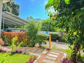 A garden pathway leading to a building entrance, surrounded by lush greenery and a variety of plants. - NatureVilla Kochi (Aluva)