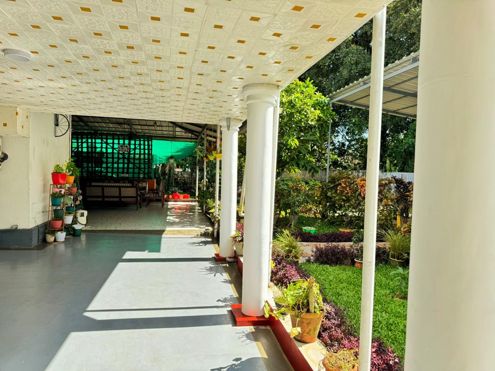 A covered walkway with a patterned ceiling, potted plants, and a view of a garden area.