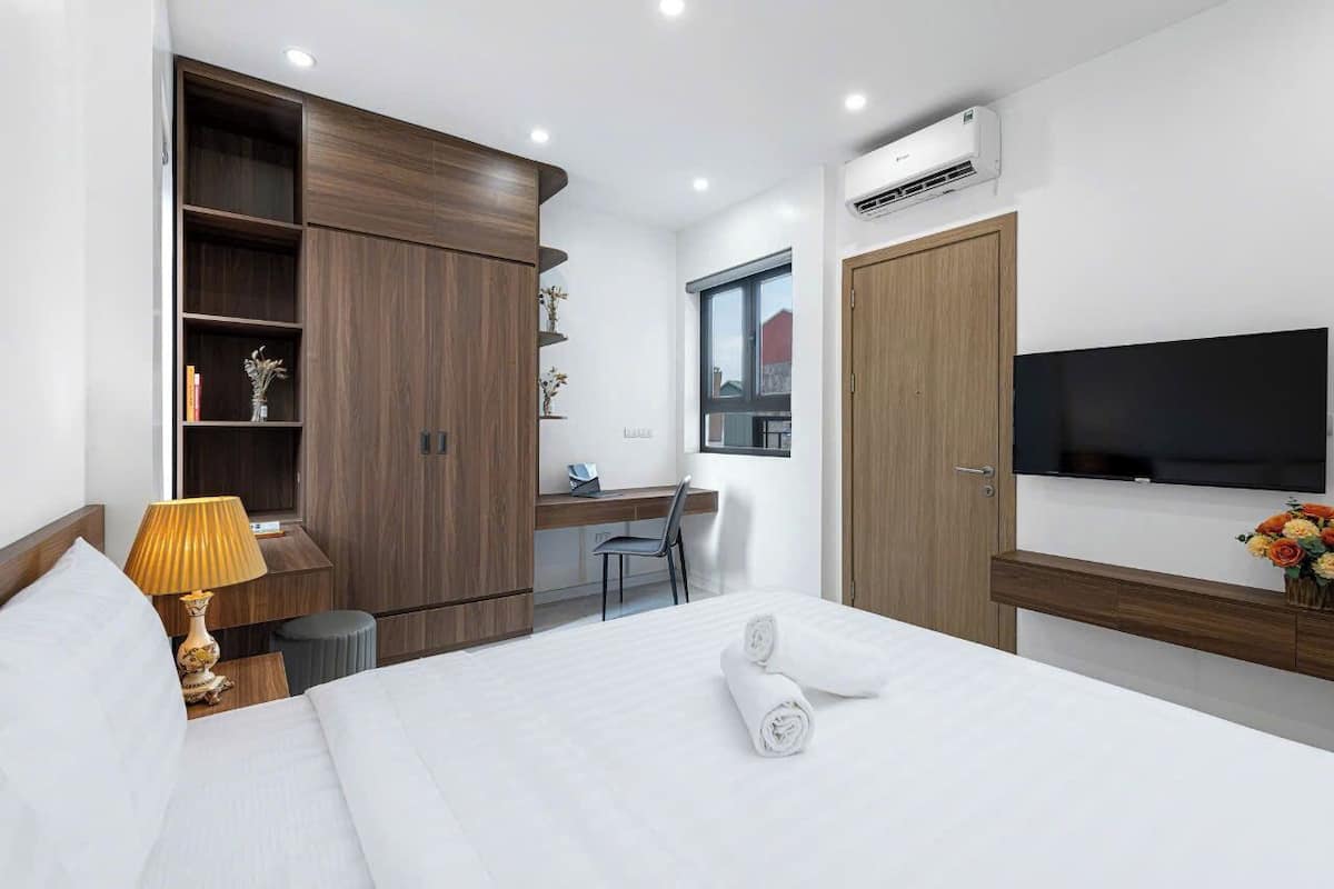 A modern hotel room with a bed, a desk, a chair, a TV, and a wardrobe.