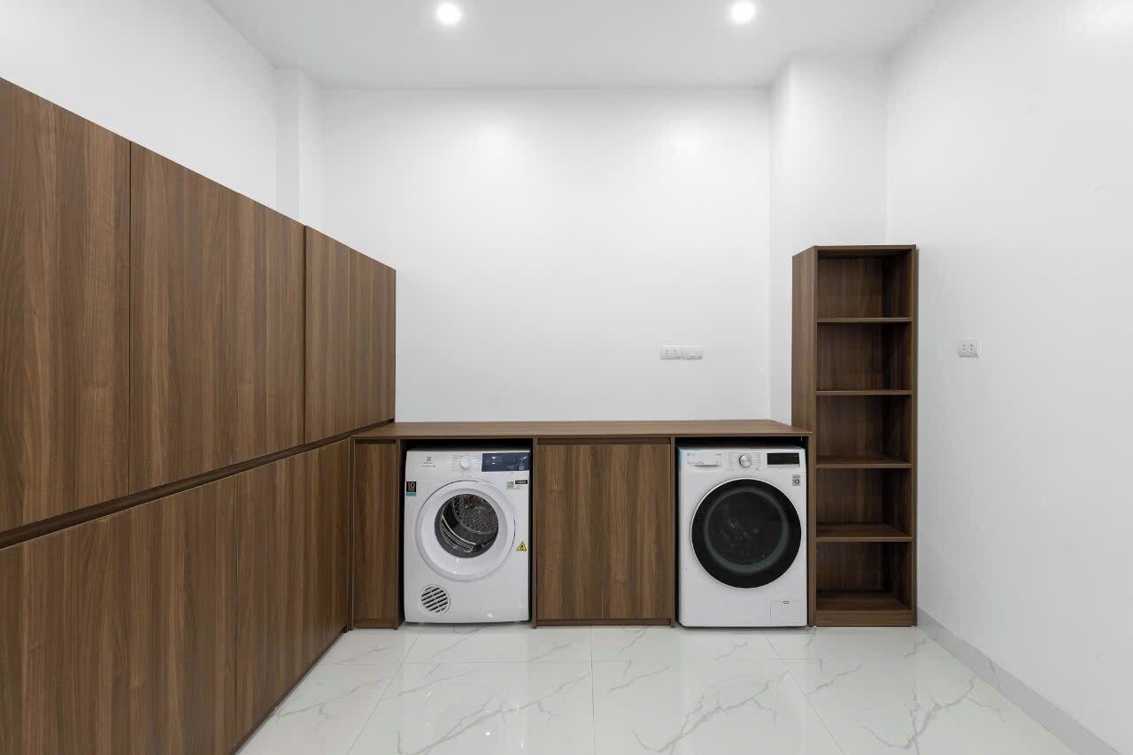 A laundry room with two washing machines, wooden cabinets, and a built-in shelf unit.