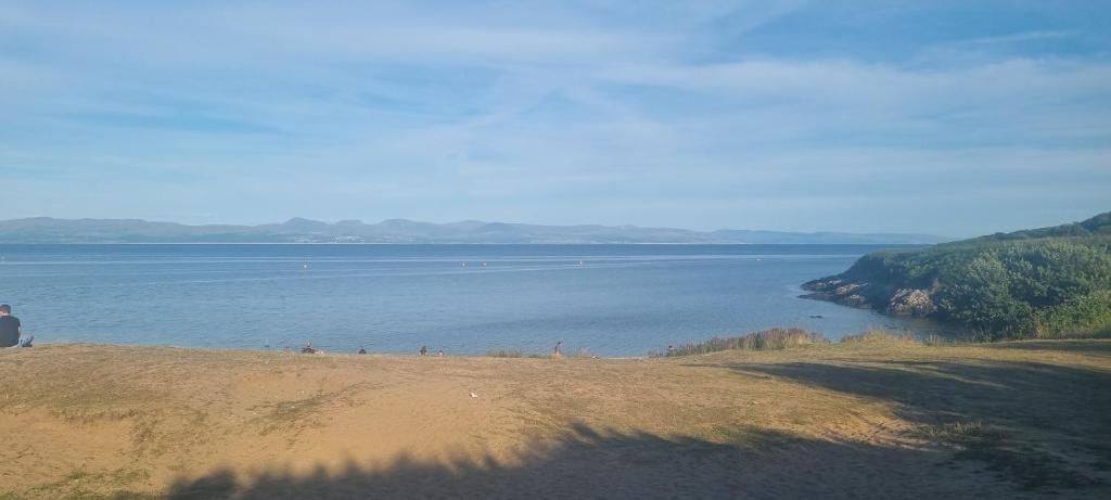 Un paisaje costero con una playa arenosa, cielo despejado y montañas a lo lejos.