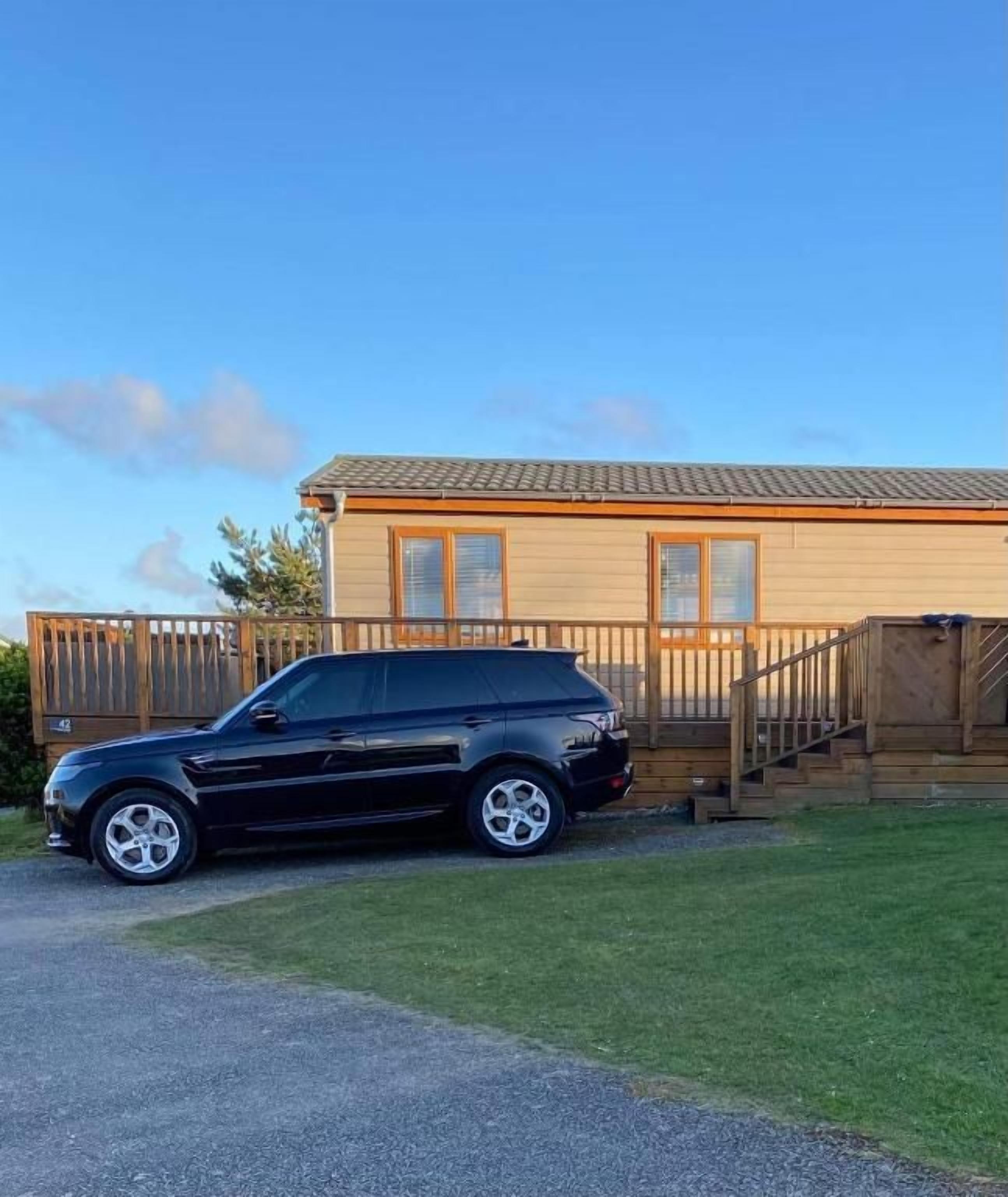 A black SUV parked in front of a wooden house with a visible staircase and a fenced yard.