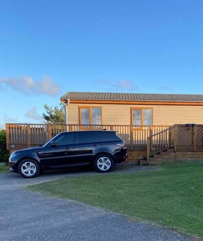 A black SUV parked in front of a wooden house with a visible staircase and a fenced yard.