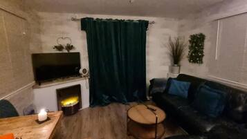 A living room with a fireplace, a sofa, a coffee table, and a television mounted on the wall.