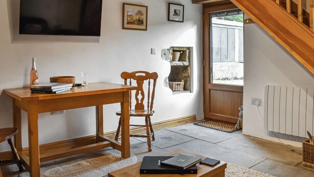 Un salon chaleureux avec une table en bois, une chaise, un téléviseur fixé au mur et un escalier menant à un autre niveau.