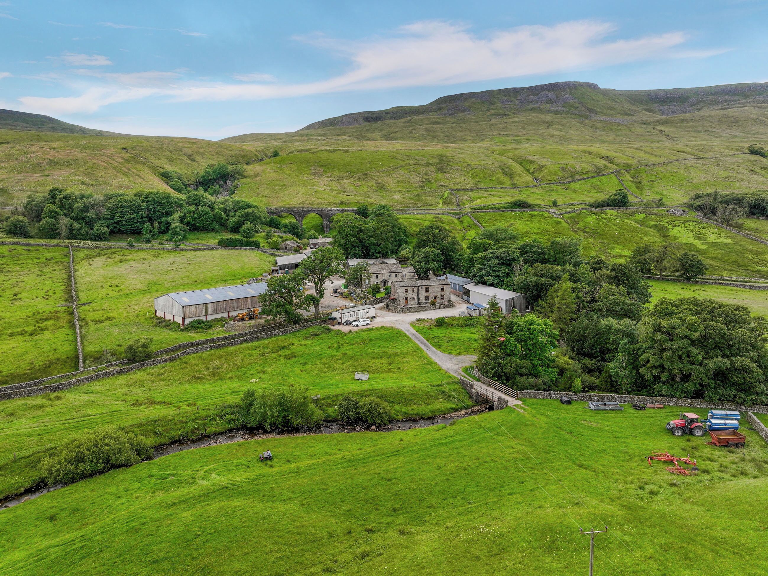 A rural landscape with a stone bridge, green fields, and a cluster of buildings.