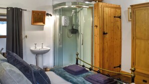 Une chambre à coucher comprenant un lit, une armoire en bois, une douche en verre et un lavabo près du lit.